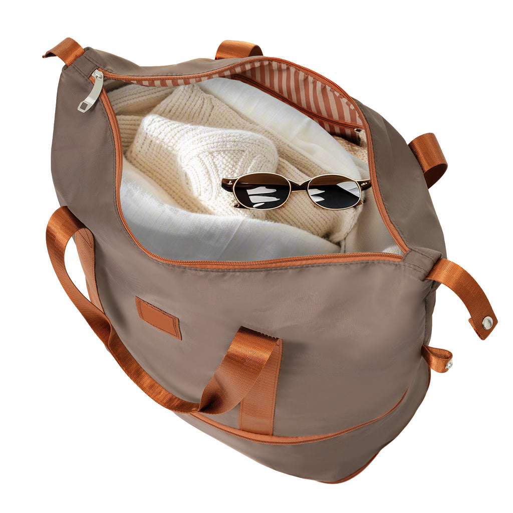 Gray duffle bag open with knit clothing and sunglasses, copper trim and side pocket