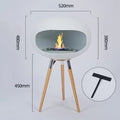 Light gray round ethanol fireplace bowl on three wood tripod legs, flame centered in tray.