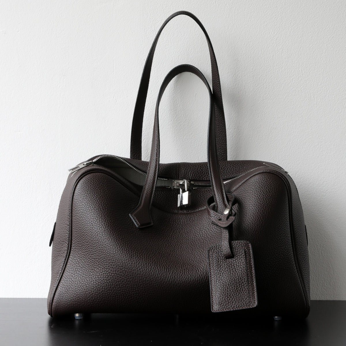 Black leather-look crossbody bag with top handles, front zipper, and hanging ID tag