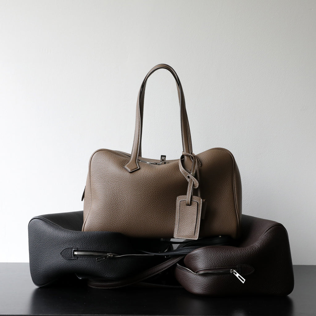 Taupe leather-look crossbody bag with top handles, front zipper, and hanging tag