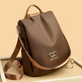 Brown backpack with curved flap, gold logo emblem, top handle and shoulder straps
