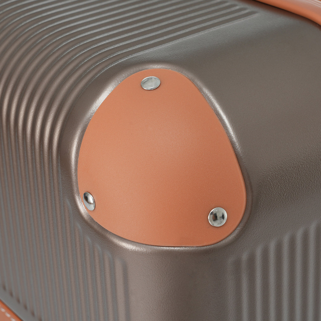 Hard-shell suitcase corner detail with coppery oval badge and metal rivets