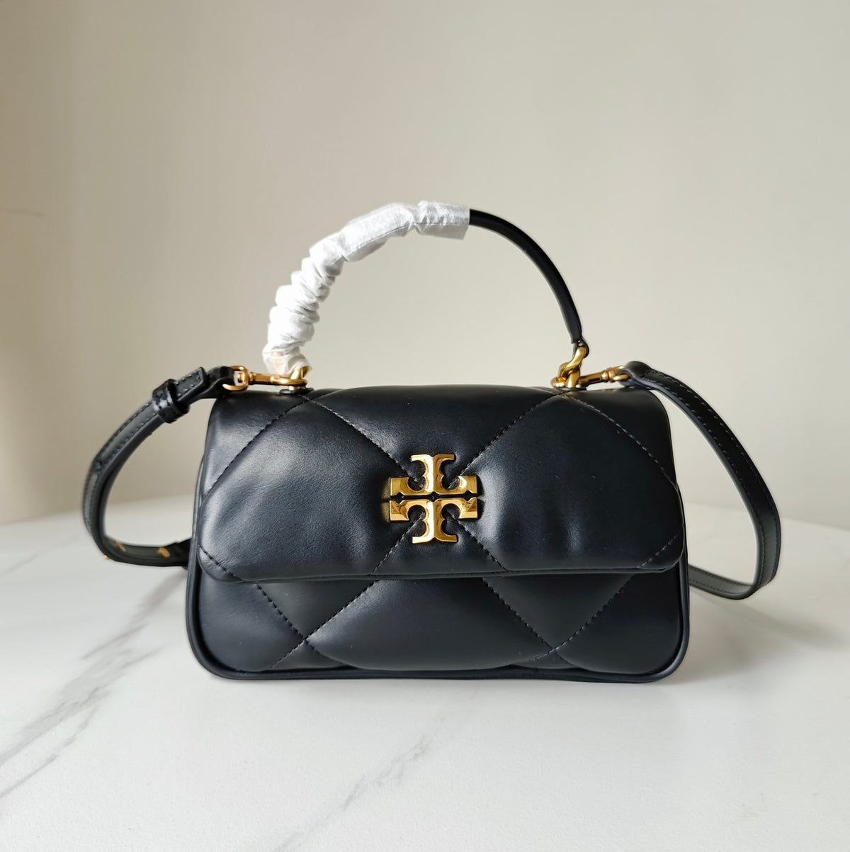 Black quilted crossbody bag with gold logo clasp, short ruched handle and shoulder strap